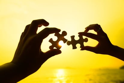 Two hands trying to connect puzzle pieces with sunset background- Improve Visibility and reporting
